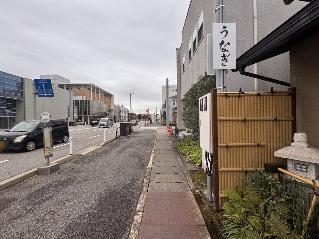 ふじさん富山店の前の歩道と「うなぎ」の縦看板、店の前のバス停